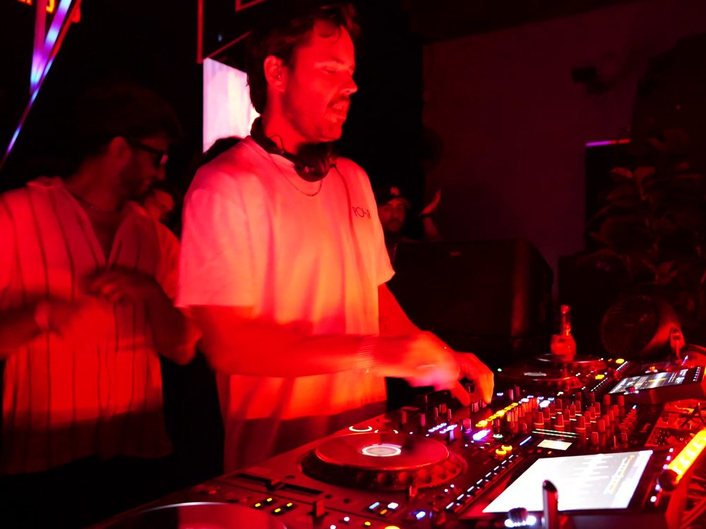 DJ at the decks surrounded by dancers under red light