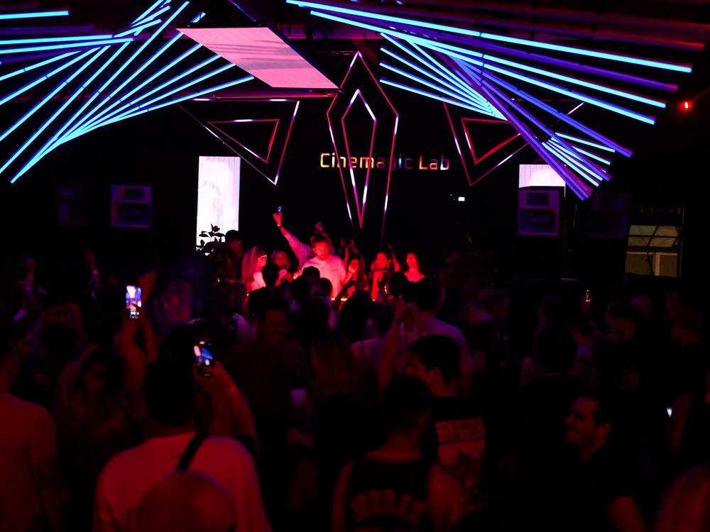 Crowd with hands raised beneath the CINEMAGIC Lab light installation